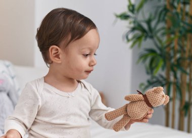 Tatlı İspanyol çocuk yatak odasında elinde oyuncak bebekle yatakta oturuyor.