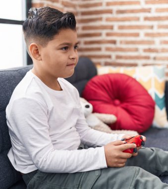 Adorable hispanic boy playing video game sitting on sofa at home