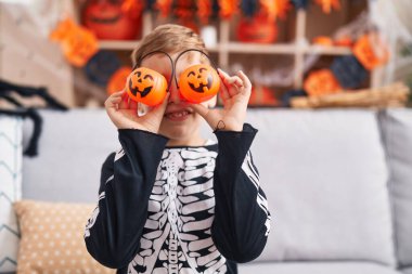 İskelet kostümlü sevimli İspanyol çocuk evde gözleri üzerinde balkabağı sepetleri tutuyor.