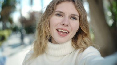 Young blonde woman smiling confident making selfie by camera at park