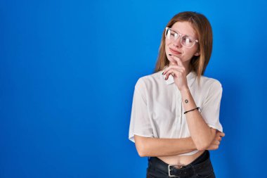 Mavi arka planda duran güzel bir kadın kameraya kendinden emin bir şekilde bakıyor kollarını kavuşturmuş ve çenesini kaldırmış gülümsüyor. Olumlu düşünmek. 