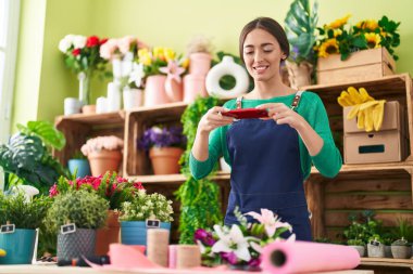 Genç ve güzel İspanyol çiçekçi çiçekçi çiçekçide çiçekçide akıllı telefonla fotoğraf çekiyor.