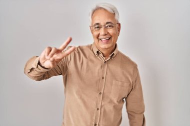 Gözlüklü, gülümseyen, parmaklarını zafer işareti yaparken gösteren İspanyol bir adam. İki numara.. 