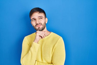 Mavi arka planda dikilen İspanyol bir adam bir soru hakkında endişeli ve gergin bir şekilde düşünüyor. 