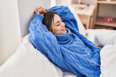 Genç, güzel, İspanyol bir kadın yatakta müzik dinliyor.