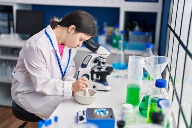 Down sendromlu genç kadın bilim adamı laboratuarda çalışırken gülümsüyor.