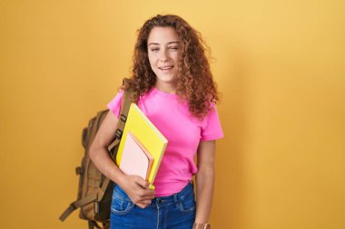 Öğrenci çantası takan, elinde kitaplarla kameraya seksi bir ifadeyle bakan beyaz bir kadın. Neşeli ve mutlu bir yüz.. 