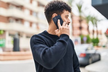 Genç Arap adam gülümsüyor, kendinden emin bir şekilde caddedeki akıllı telefondan konuşuyor.