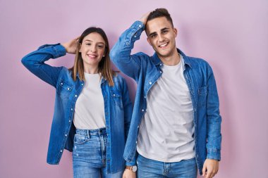 Pembe arka planda duran genç İspanyol çift gülümsüyor. Saçlarına dokunuyor, el hareketi yapıyor, çekici ve modaya uygun poz veriyor. 