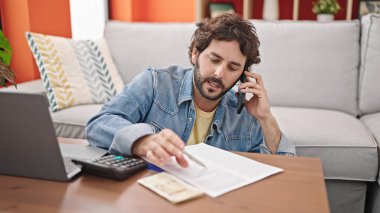Genç İspanyol adam akıllı telefondan konuşuyor. Danimarka Krone 'un evdeki muhasebe sözleşmesini imzalıyor.