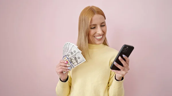 Young Blonde Woman Using Smartphone Holding Dollars Isolated Pink Background — 图库照片