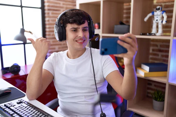 若いです非二進数の男再生ビデオゲームともにスマートフォン指す親指アップへザ側笑顔幸せとともにオープン口 — ストック写真