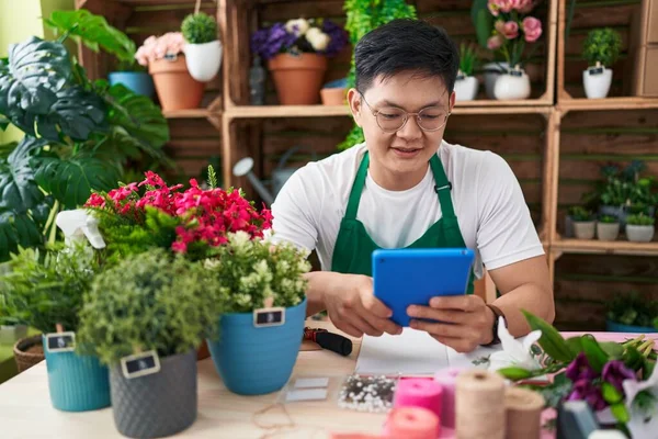 Young chinese man florist smiling confident using touchpad at flower shop