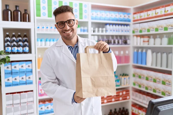 Joven Farmacéutico Hispano Sonriendo Confiado Sosteniendo Bolsa Compras Farmacia —  Fotos de Stock