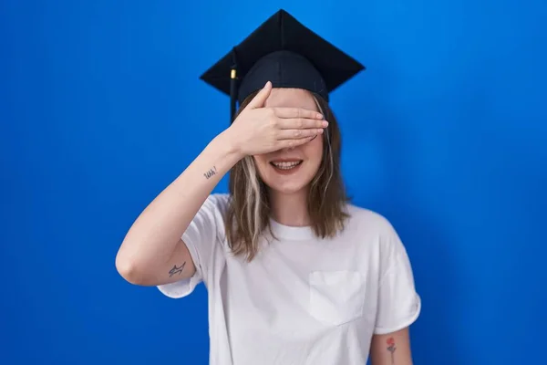 卒業キャップを被った金髪の白人女性は笑顔で 驚きのために目を覆う顔で手で笑っています 視覚障害の概念 — ストック写真