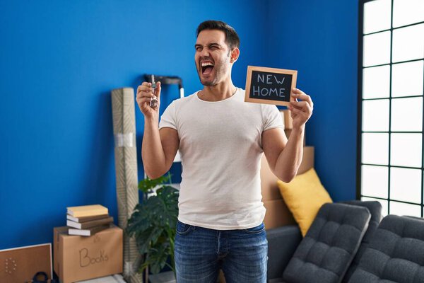 Молодой латиноамериканец с бородой, держащий ключи от нового дома злой и безумный кричащий расстроенный и разъяренный, кричащий от гнева. гнев и агрессивная концепция. 