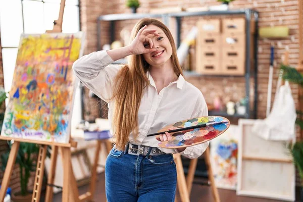 stock image Young caucasian woman at art studio holding palette smiling happy doing ok sign with hand on eye looking through fingers 