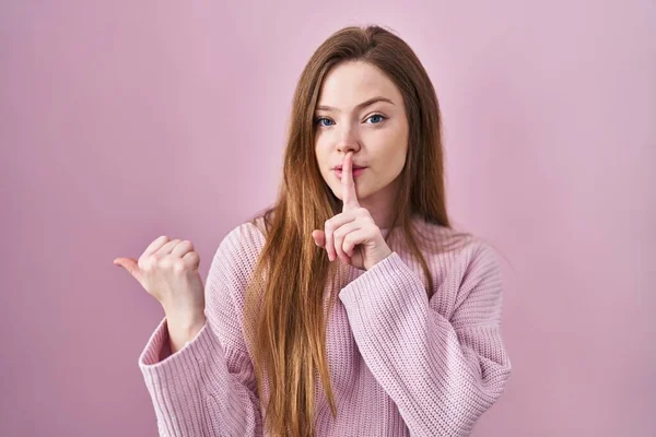 ピンクの背景の上に立つ若い白人女性は 唇に手で側に指して指で静かにするように求めている 沈黙と秘密の概念 — ストック写真