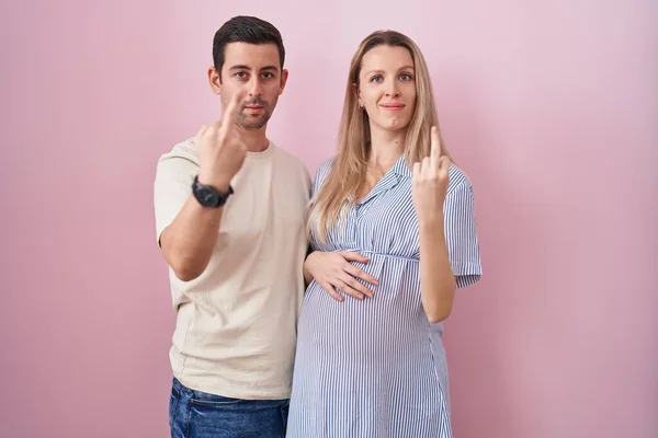 Young Couple Expecting Baby Standing Pink Background Showing Middle Finger — Fotografia de Stock