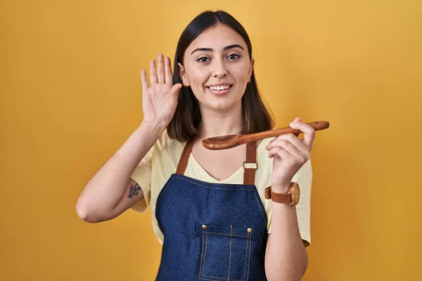 ヒスパニック系の女の子健康的な木製のスプーンを食べることはこんにちは幸せと笑顔 優しい歓迎ジェスチャーを言って放棄 — ストック写真