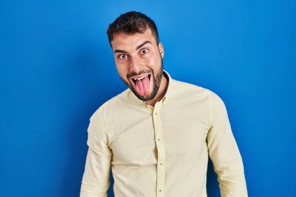 面白い表情で嬉しそうに舌を突き出している青い背景に立つハンサムなヒスパニック系の男 感情の概念 — ストック写真
