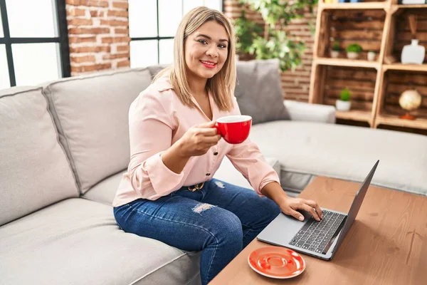 Young Hispanic Woman Using Laptop Drinking Coffee Sitting Sofa Home — Stock fotografie