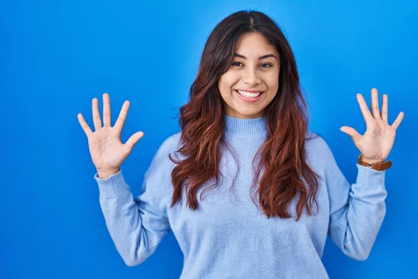 西班牙裔年轻女子站在蓝色的背景上 带着自信和快乐的微笑 用十号手指指指着 — 图库照片