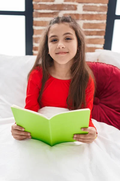 愛らしいHispanic女の子読書本座っています上のベッドルームで — ストック写真