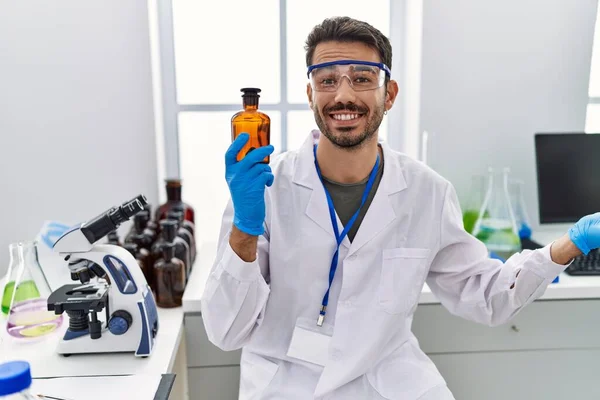 Молодой Латиноамериканец Работающий Лаборатории Ученого Держит Бутылку Радостной Улыбкой Выражением — стоковое фото