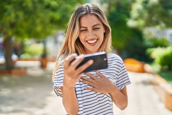 年轻的金发女人笑着自信地在公园看智能手机上的视频 — 图库照片