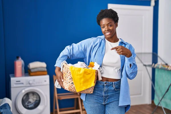 stock image African american woman holding laundry basket pointing finger to one self smiling happy and proud 