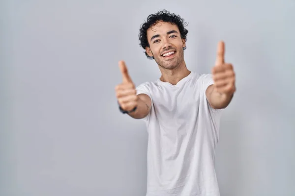孤立した背景の上に立つヒスパニック系の男は 手で積極的なジェスチャーを行うことを承認します 親指アップ笑顔と成功のために幸せ 勝者のジェスチャー — ストック写真