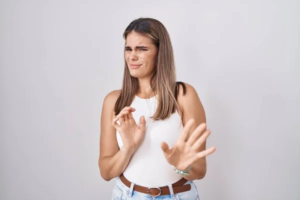 Hispanic young woman standing over white background disgusted expression, displeased and fearful doing disgust face because aversion reaction.