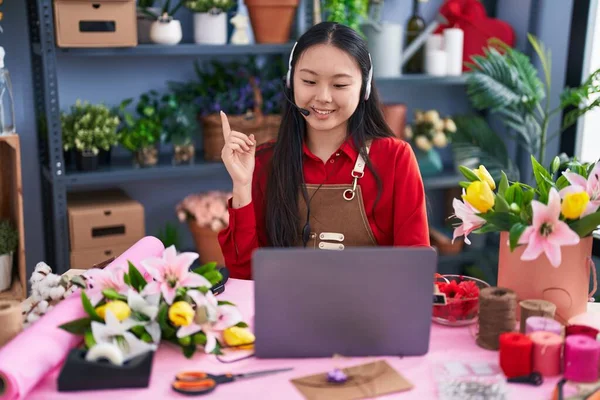 Young asian woman working at florist shop doing video call smiling happy pointing with hand and finger to the side