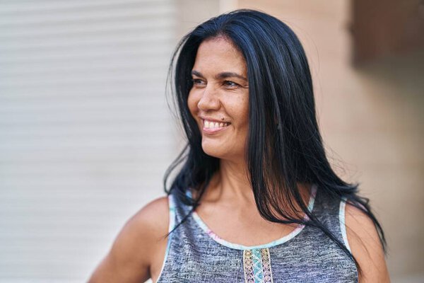 Латиноамериканка средних лет улыбается уверенно глядя в сторону улицы