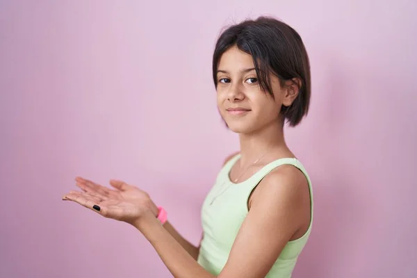 年轻姑娘站在粉红的背景上 手拉手放在一边 展示复制的空间 呈现广告时面带微笑 高兴极了 — 图库照片