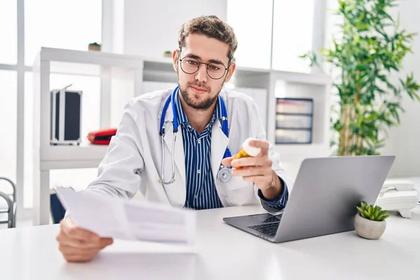 Young Man Doctor Reading Medical Report Holding Pills Clinic — Stockfoto