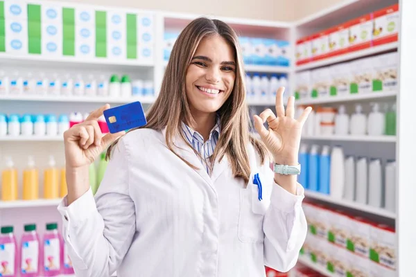 Mujer Joven Hispana Trabajando Farmacia Sosteniendo Tarjeta Crédito Haciendo Signo — Foto de Stock