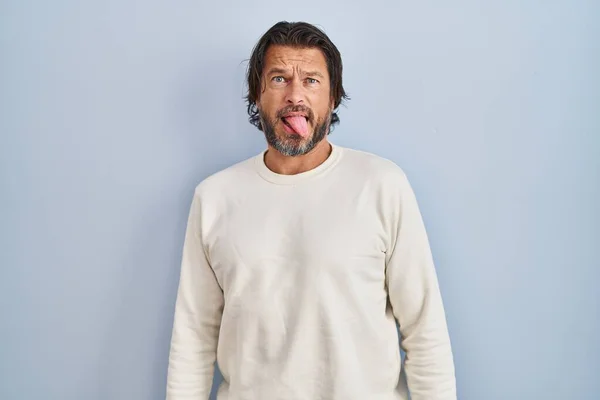 青い背景にカジュアルなセーターを着たハンサムな中年男性が面白い表情で幸せ舌を突き出しています 感情の概念 — ストック写真