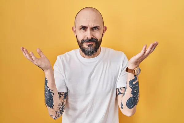 Young Hispanic Man Tattoos Standing Yellow Background Clueless Confused Expression —  Fotos de Stock