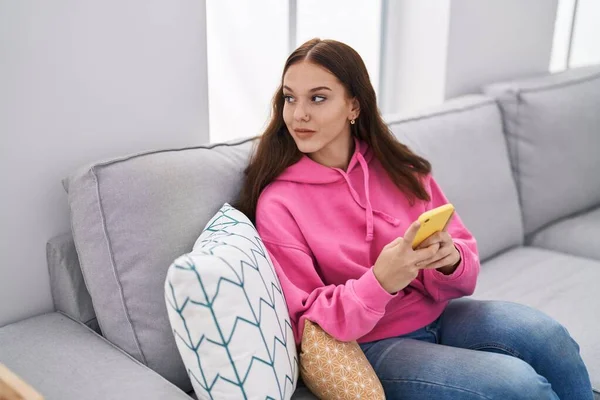Młoda Kobieta Przy Użyciu Smartfona Siedząc Kanapie Domu — Zdjęcie stockowe