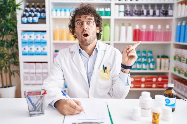Hispanic Young Man Working Pharmacy Drugstore Surprised Pointing Finger Side — Stock Photo, Image