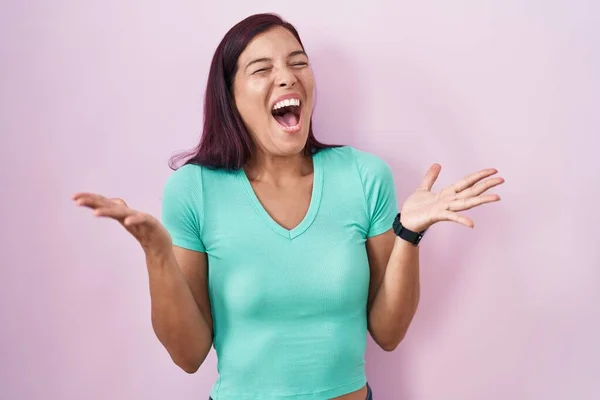 ピンクの背景の上に立つ若いヒスパニック系の女性は 狂気を祝い 腕を上げて興奮して叫んで目を開けて成功に驚いています 勝者のコンセプト — ストック写真