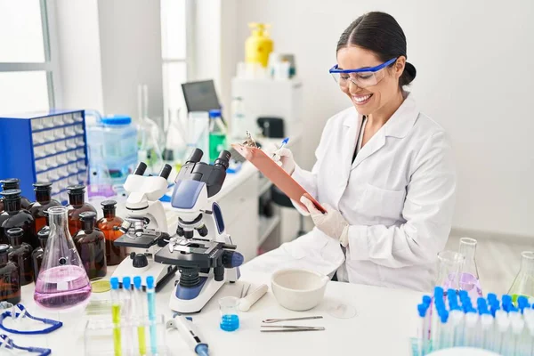 年轻美丽的惊慌失措的女科学家微笑着写着自信的报告在实验室工作 — 图库照片