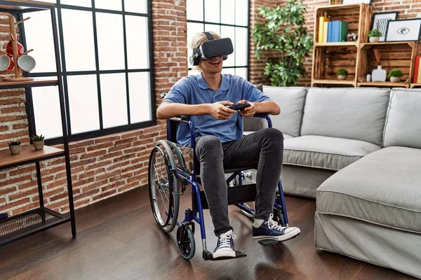 若いですブロンド男遊びビデオゲーム使用して仮想現実眼鏡とジョイスティック上の車椅子に家に座って — ストック写真