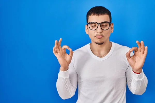 年轻的阿拉伯男子穿着宽松的白色衬衫和眼镜 闭着眼睛 用手指做冥想动作 瑜伽概念 — 图库照片