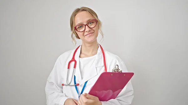 Joven Mujer Rubia Médico Sonriendo Confiado Sujetando Portapapeles Sobre Fondo —  Fotos de Stock