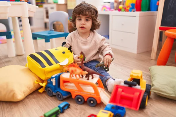 stock image Adorable hispanic boy playing with car and dinosaur toy sitting on floor at kindergarten