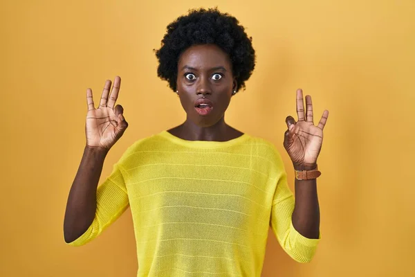 黄色のスタジオの上に立っているアフリカの若い女性は驚きと指でOk承認シンボルをやってショックを受けました クレイジーな表現 — ストック写真