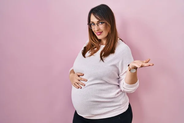 Těhotná Žena Stojící Nad Růžovým Pozadím Úsměvem Veselý Prezentaci Ukazuje — Stock fotografie